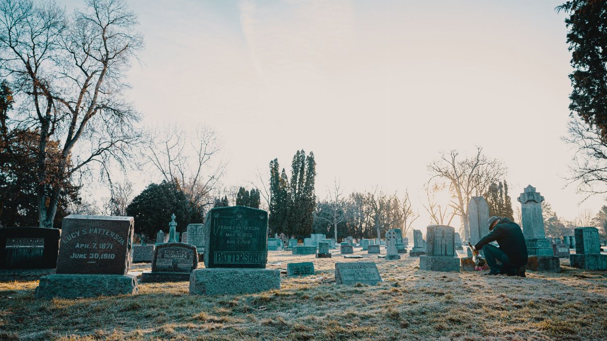 A serene cemetery at sunrise with a person reflecting by a gravestone