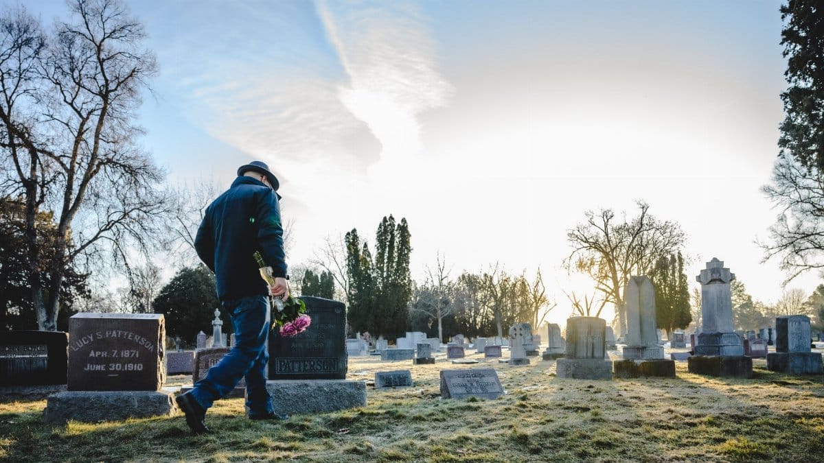 A person carrying flowers walks through a cemetery at sunrise, creating a serene and reflective scene.