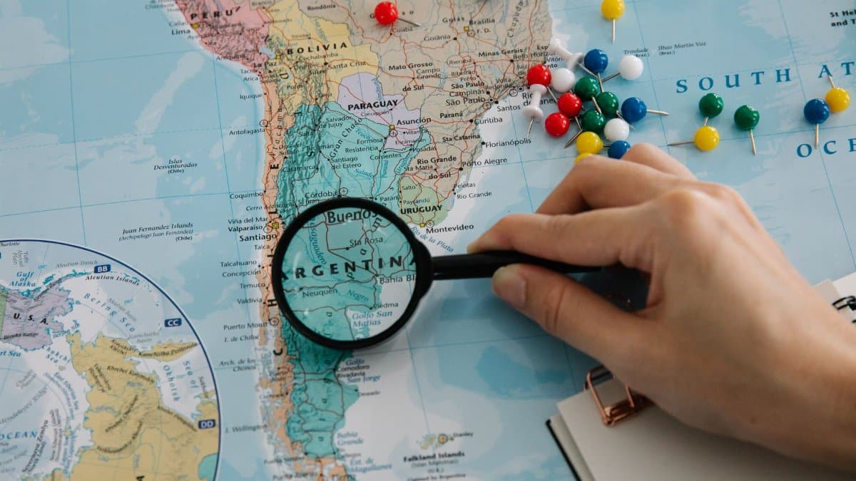 Close-up of a hand examining a South America map with a magnifying glass, highlighting Argentina.