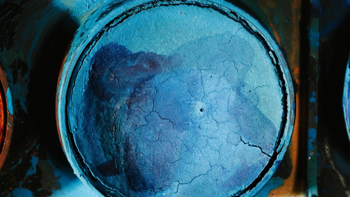 Detailed view of a cracked blue paint coating on a metal surface, showing texture and color variation.