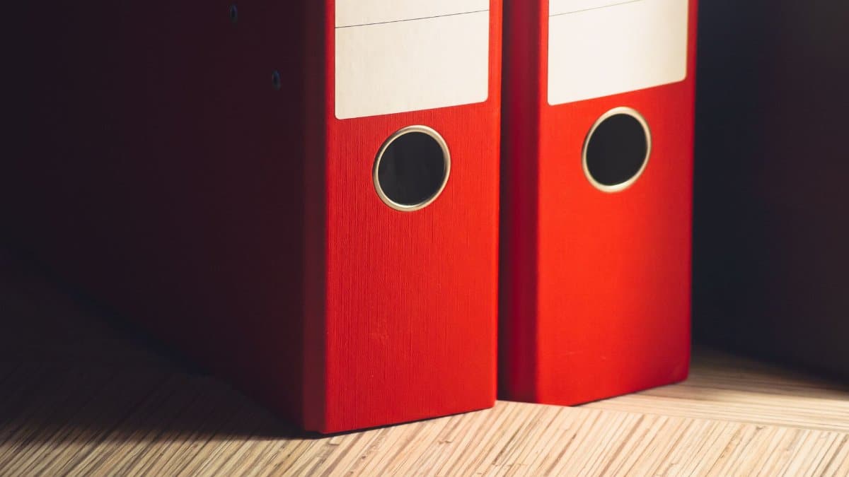 Close-up of two red lever arch files on a wooden desk in a modern office setting.