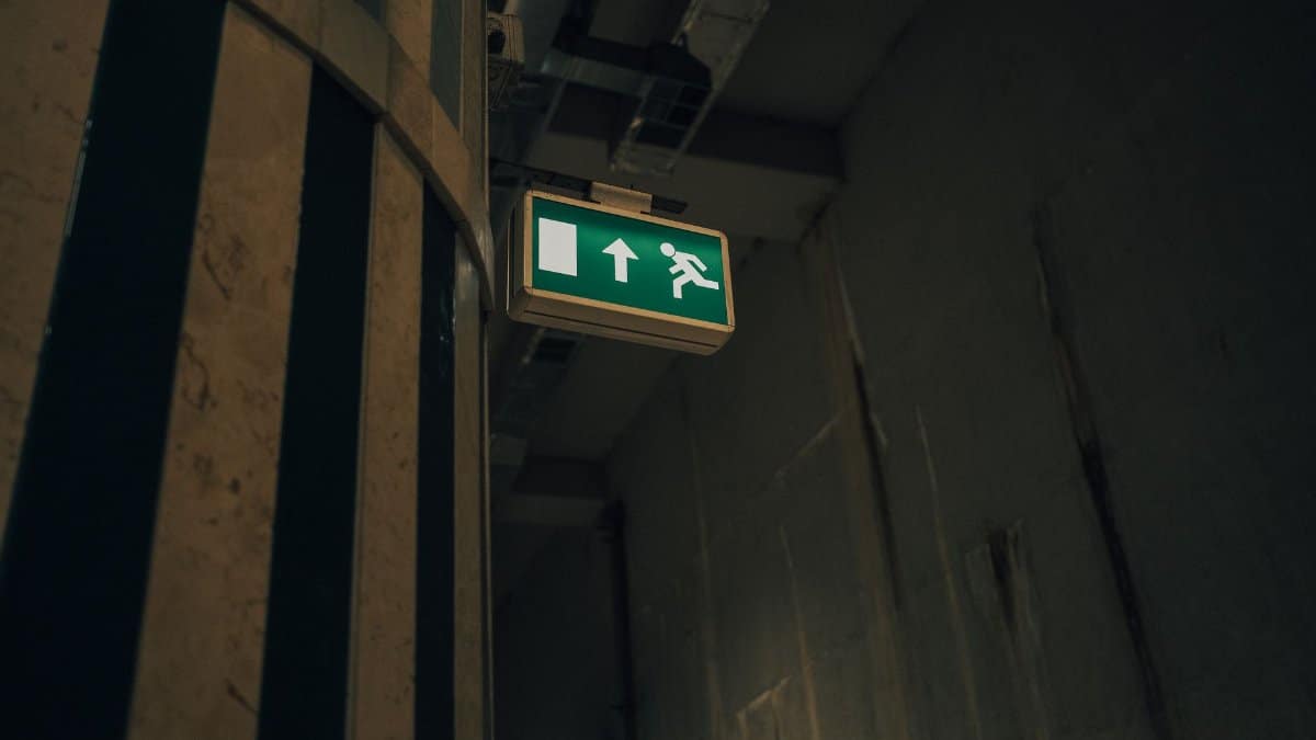 A dimly lit corridor with a green and white emergency exit sign indicating direction.