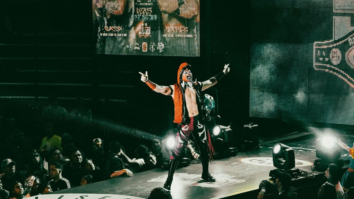 A vibrant luchador performs on stage in a lively wrestling event, thrilling a packed audience.