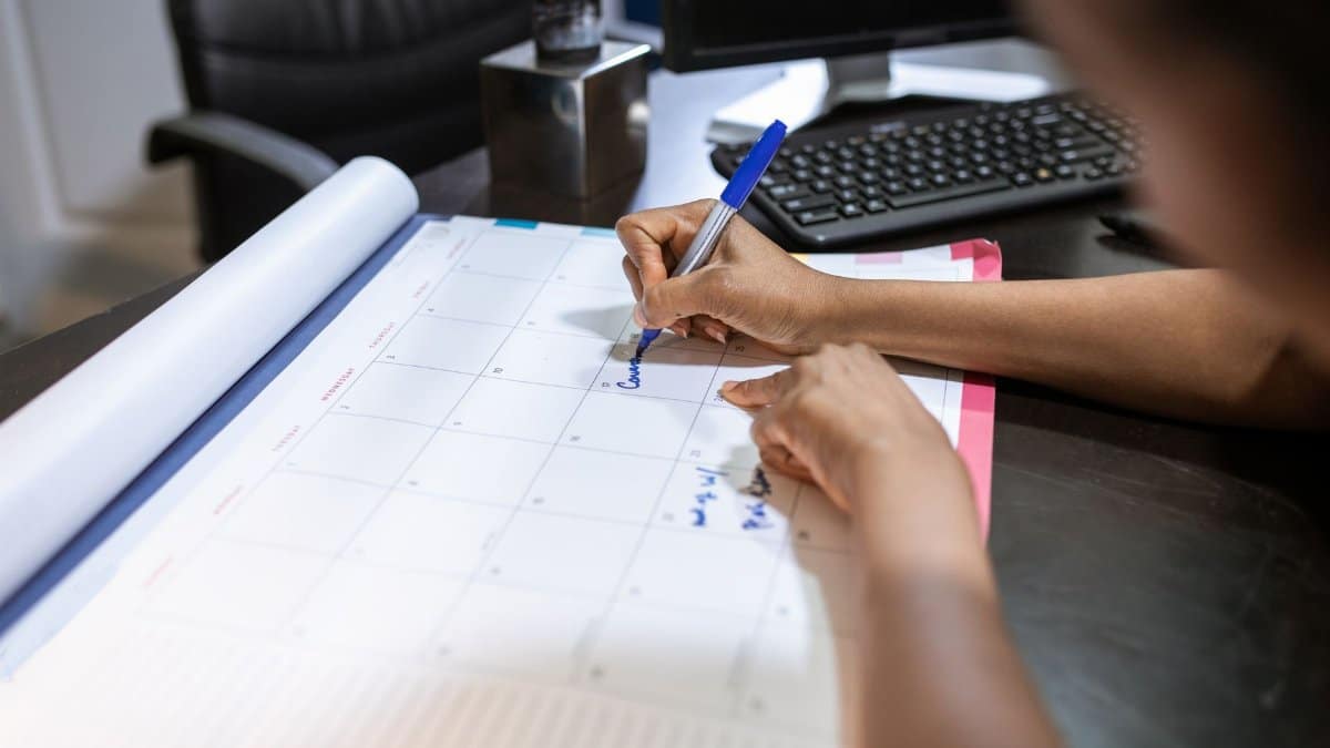 Close-up of a woman planning her schedule on a desk calendar in an office setting.