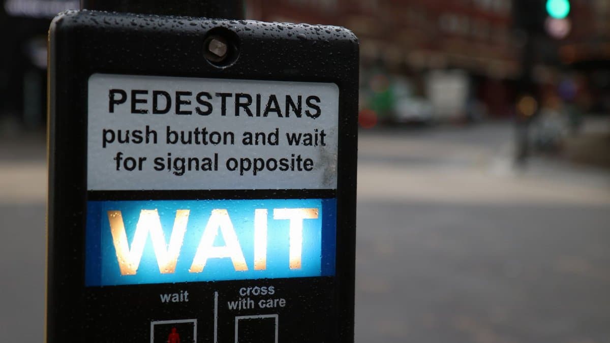 Close-up of a pedestrian crossing button with 'Wait' sign in a rainy London street.