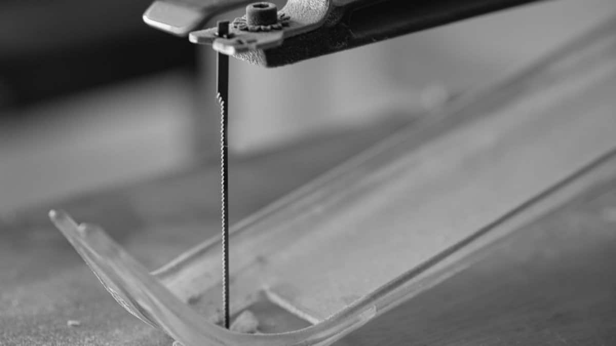 Detailed black and white image of a scroll saw blade positioned for cutting plastic.