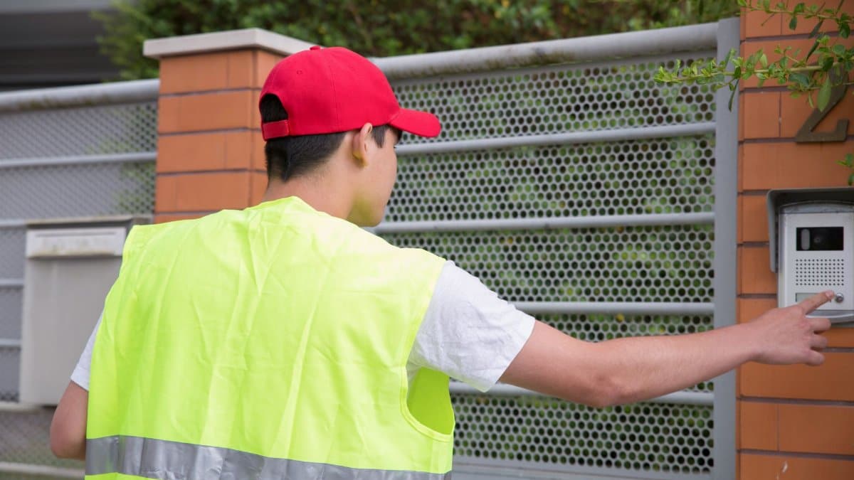 Courier in safety vest rings residence doorbell, view from behind.