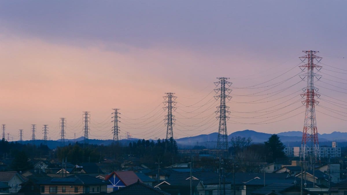 A suburban scene at dusk featuring rows of power lines and distant mountains under a colorful sky.