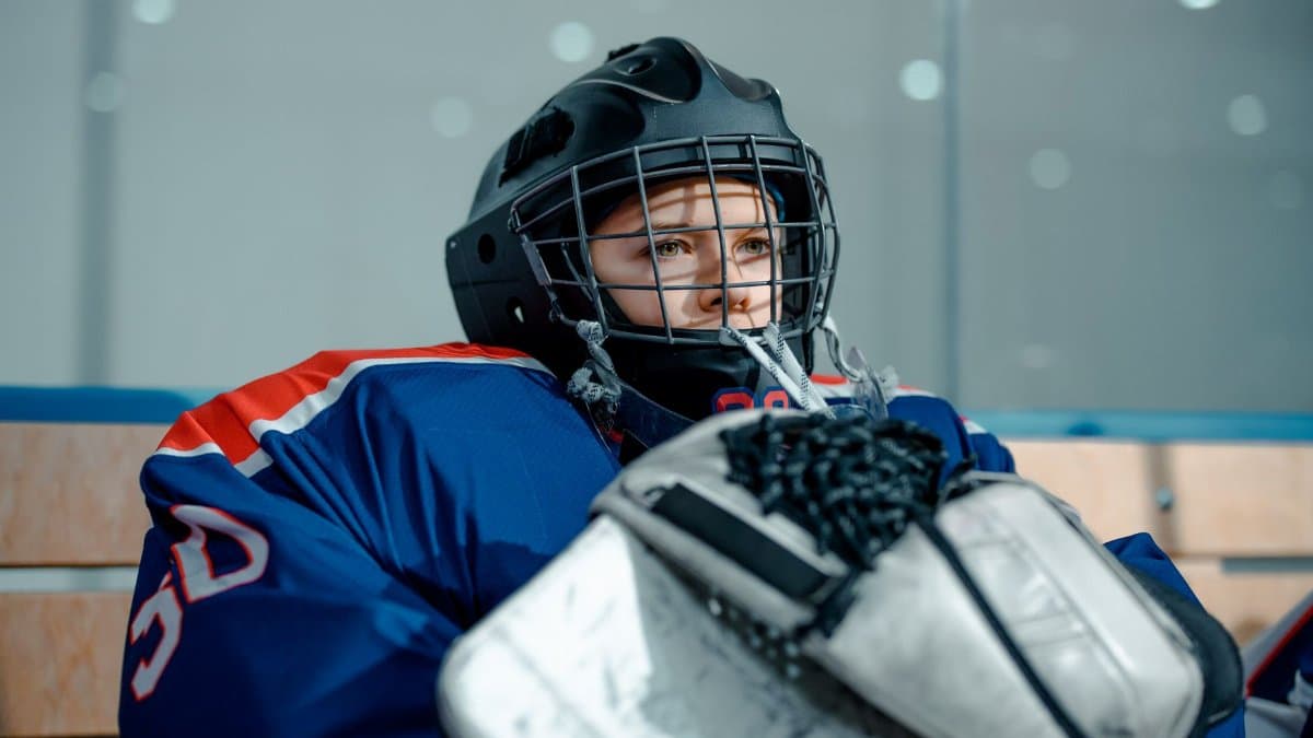 Ice hockey goalie in gear sitting on the bench indoors, concentrating before a game.