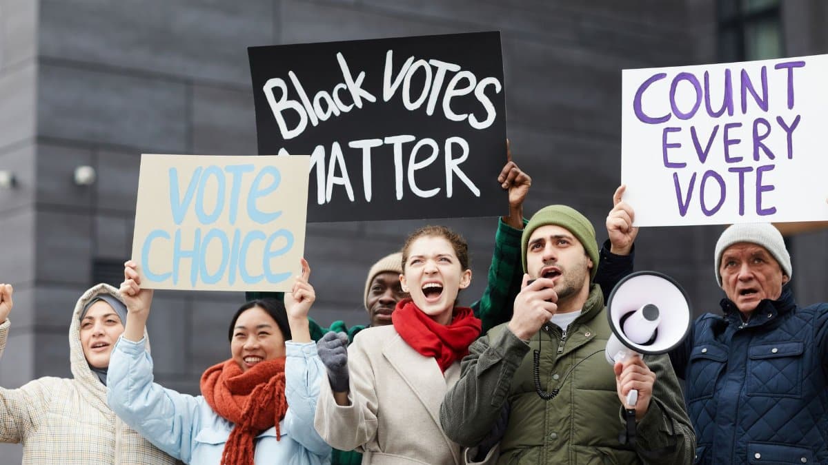 A diverse group of people protesting for voting rights with signs and megaphone outdoors.