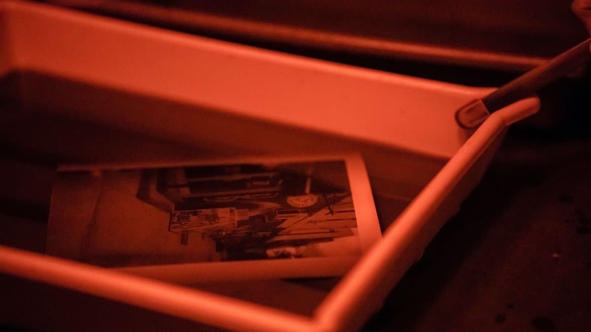 Monochrome photo in a developing tray with red light, showcasing darkroom process.