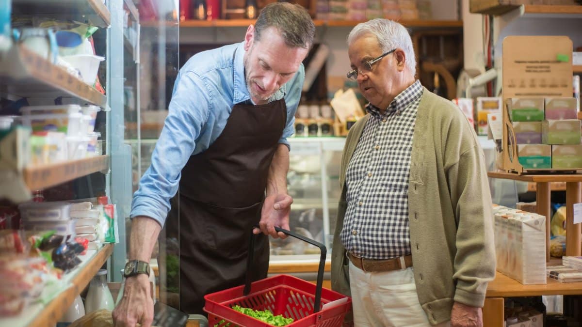 A salesman helps an elderly man with shopping in a local grocery store.