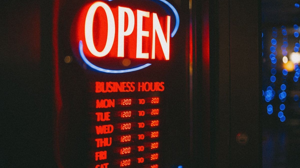 Bright neon open sign displaying business hours, glowing against a dark background.