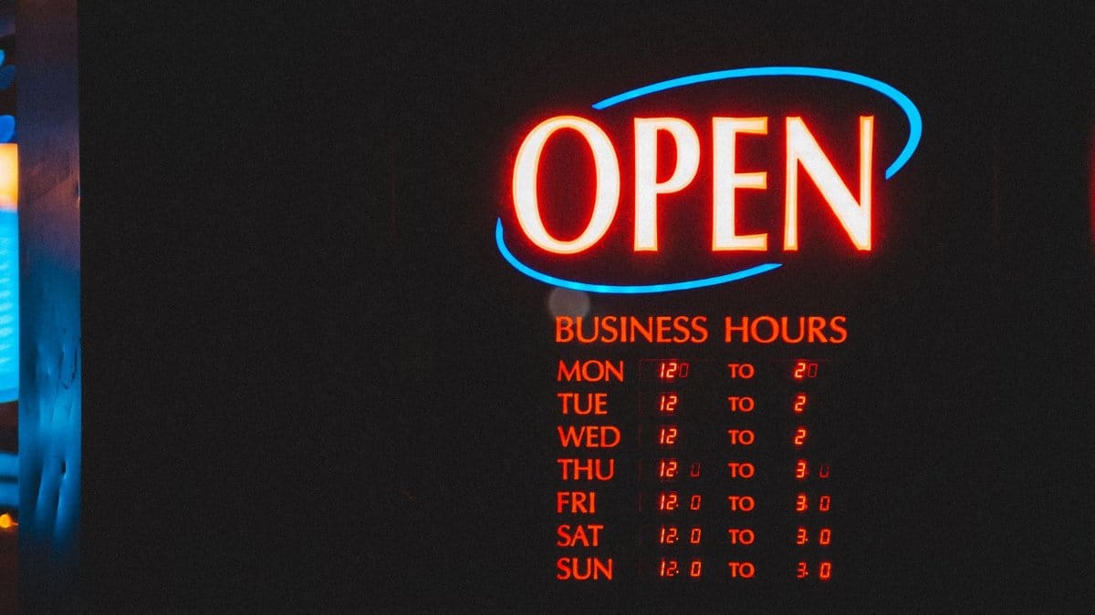 LED open sign with glowing business hours and flashing effects depicted on black board on street in city on evening time