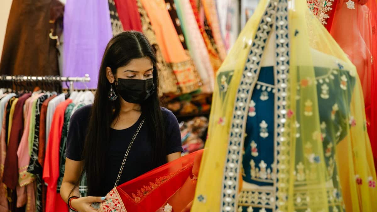 A woman wearing a face mask shops for traditional attire in a vibrant boutique.