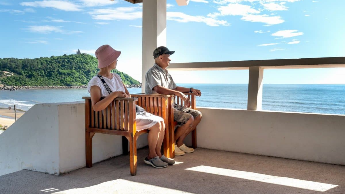 Senior couple sitting on balcony chairs, enjoying a relaxing ocean view in summer.