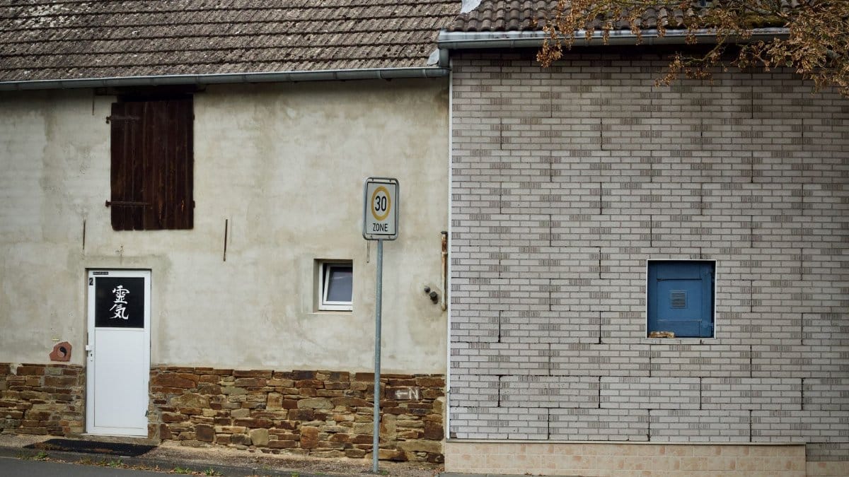 A quiet street scene featuring two distinct brick walls with a speed limit sign and doorway.