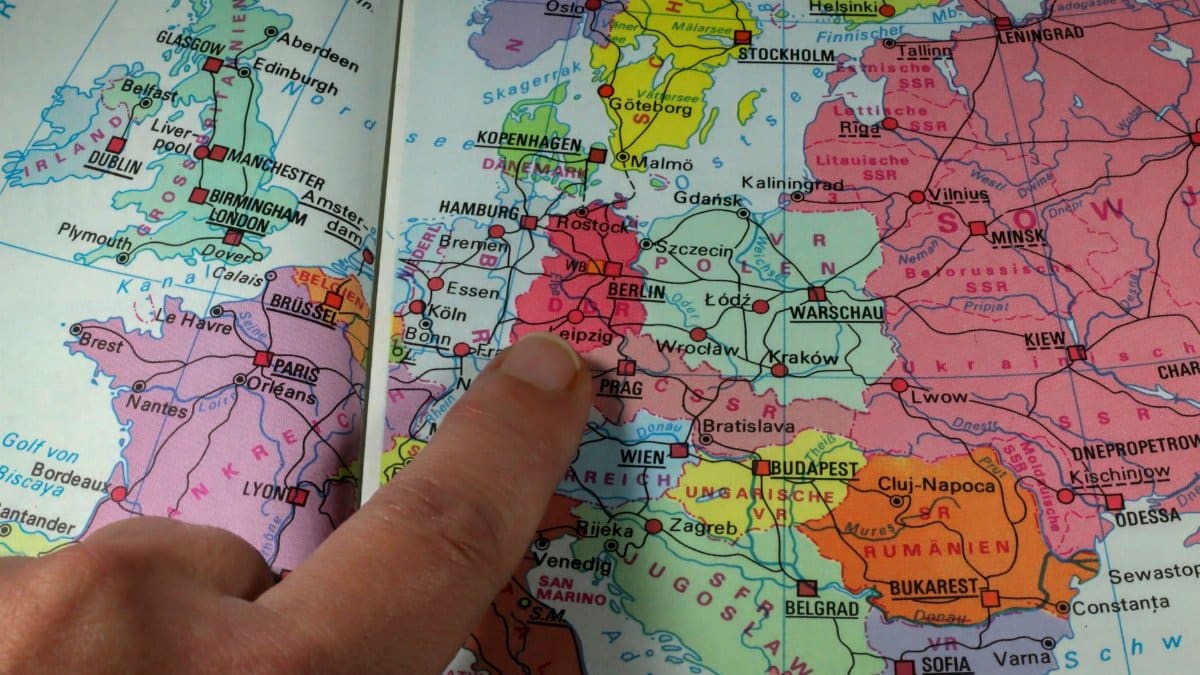 A finger points to Berlin on a colorful political map of Europe during the Cold War era.
