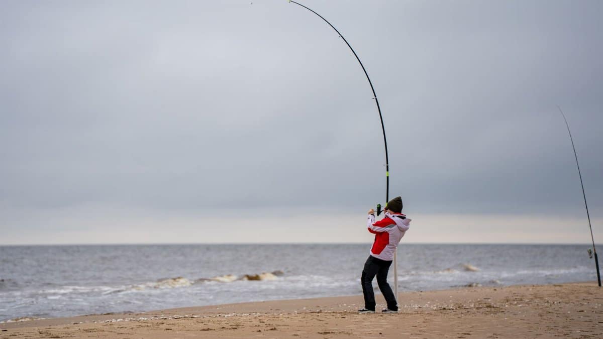 Angler enjoying fishing on the sandy coast of Latvia under a cloudy sky.