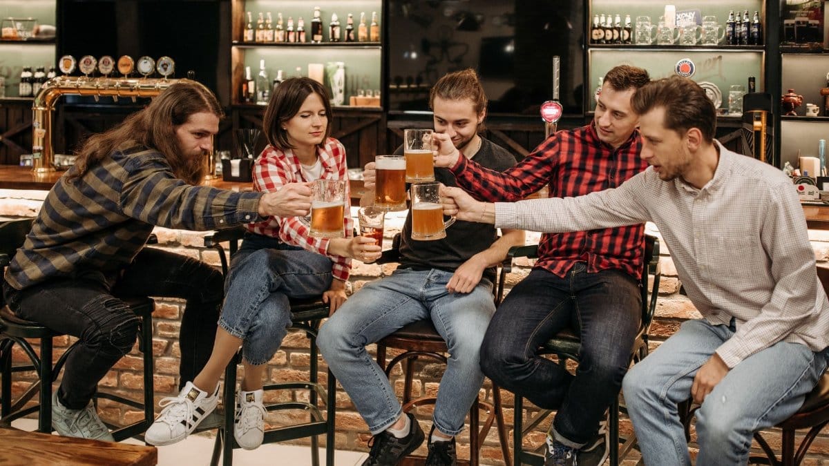 Five friends enjoying a toast with beer mugs at a cozy pub setting indoors.