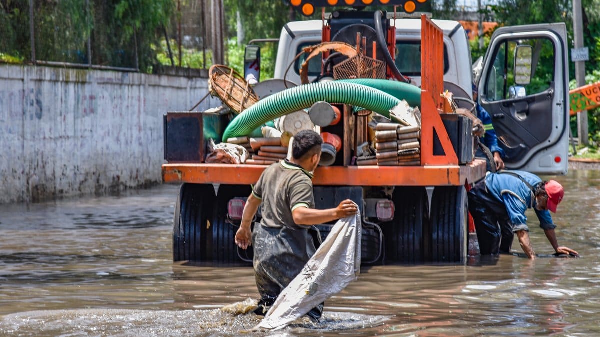 Workers wading through floodwaters near a truck, managing a city crisis after heavy rain.