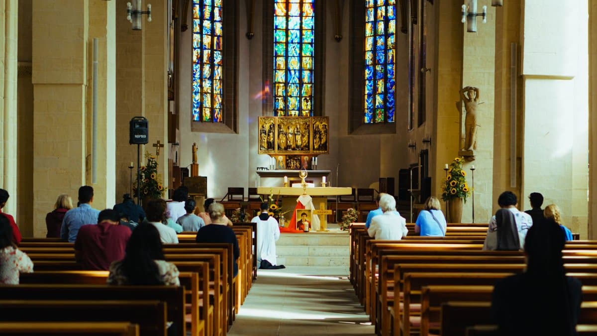 Congregation attending a service in a church with vibrant stained glass windows.