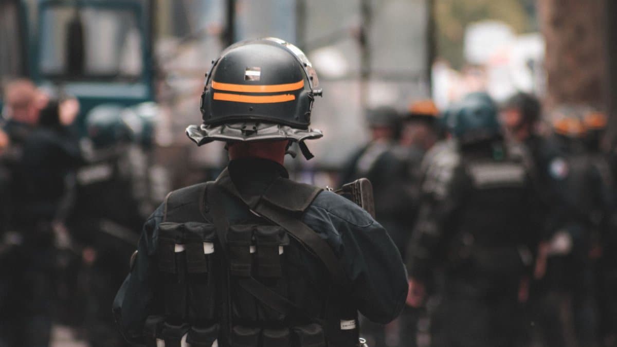 Back view of anonymous policeman in helmet and bulletproof vest maintaining law and order while standing on city street