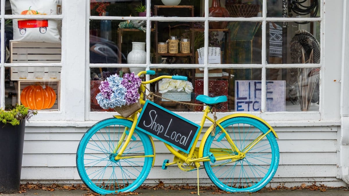 A colorful bicycle with flowers and 'Shop Local' sign outside a store in Sudbury, MA.