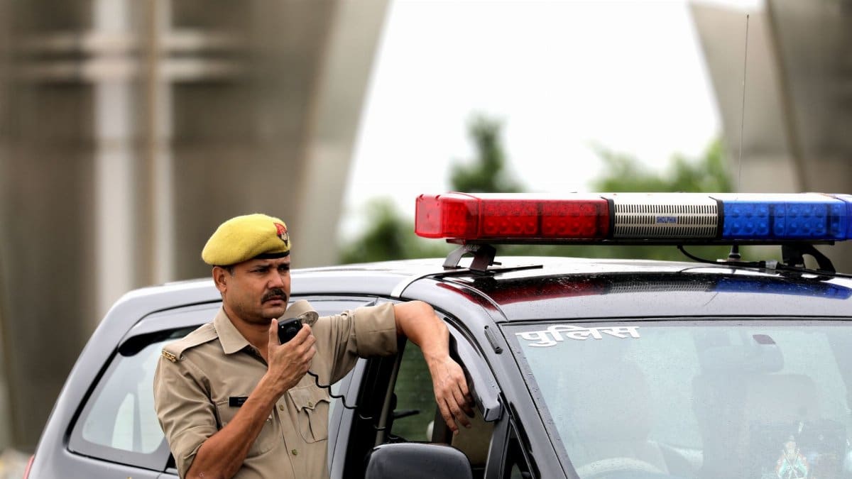 Police officer standing beside patrol car holding a radio microphone outdoors.