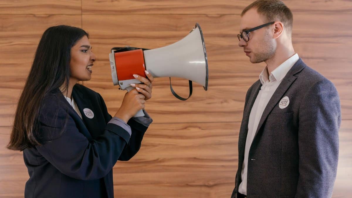A woman using a megaphone to confront a man in a suit indoors, symbolizing political debate.