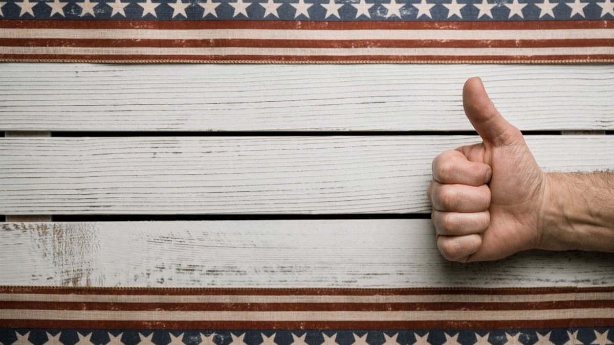 Overhead view of crop unrecognizable male with approve gesture on wooden table between American decoration with stripes and stars
