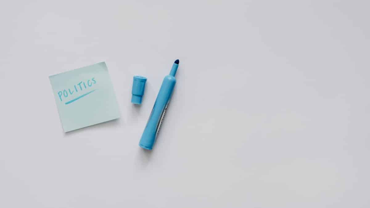 A flat lay of a blue marker and sticky note with 'politics' on a white surface.