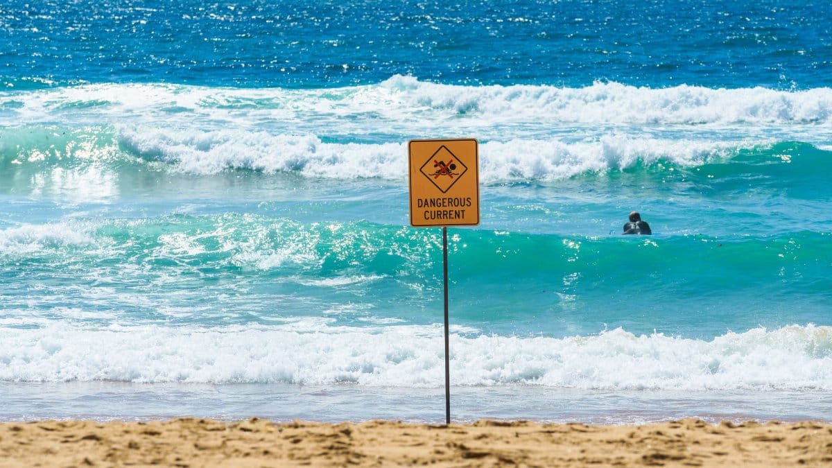 Beach scene with ocean waves and a warning sign for dangerous currents in Australia.