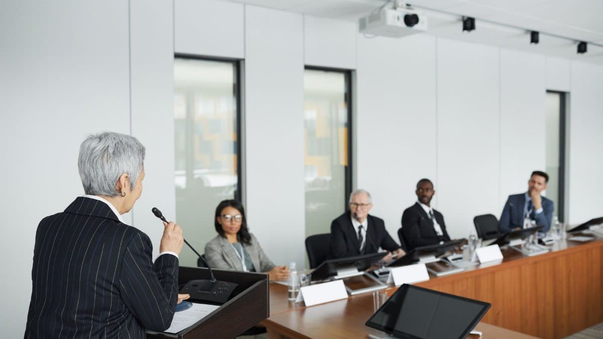 A diverse group of professionals engaging in a business meeting in a conference room with a speaker at the podium.