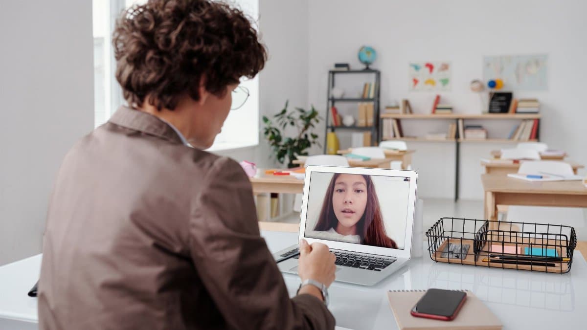 A teacher engages in an online class from an empty classroom, using a laptop for learning.