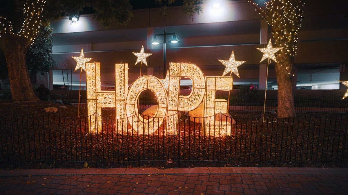 A glowing 'Hope' sign adorned with stars and lights creates a festive atmosphere in a city park at night.
