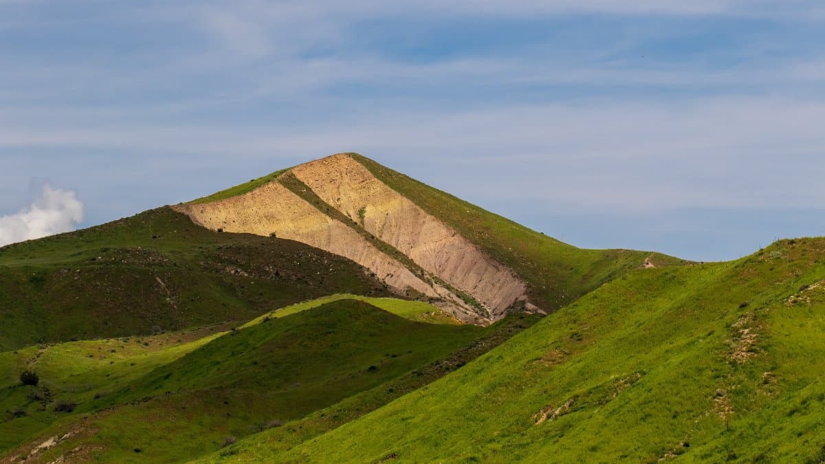 A picturesque landscape of lush green hills and a sunlit mountain under a clear blue sky.