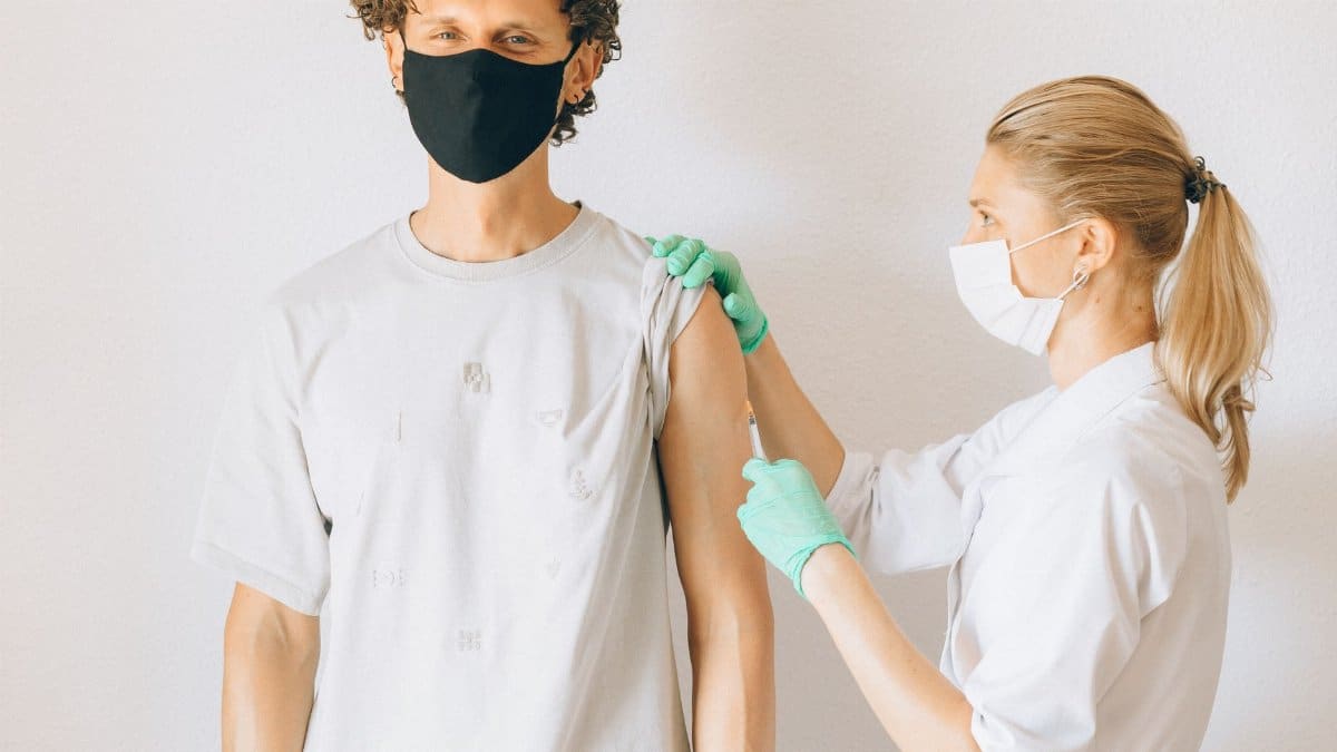 A healthcare worker giving a vaccine injection to a masked man in a clinic.