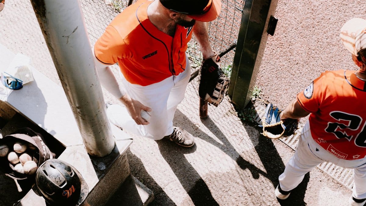 Overhead shot of two baseball players in a dugout wearing orange uniforms, ready for the game.