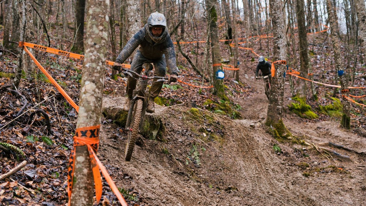 Riders tackle a challenging, muddy course during a forest mountain bike race, showcasing skill and endurance.