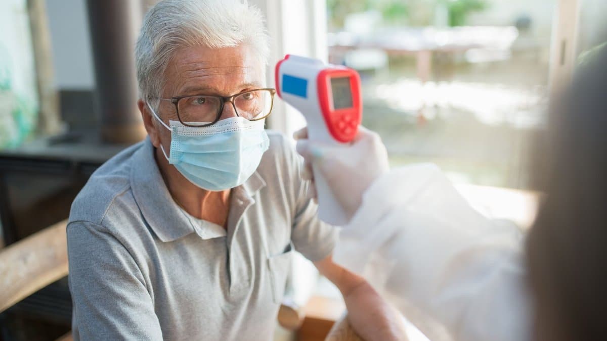 Elderly man wearing a face mask having his temperature checked indoors with a contactless thermometer.