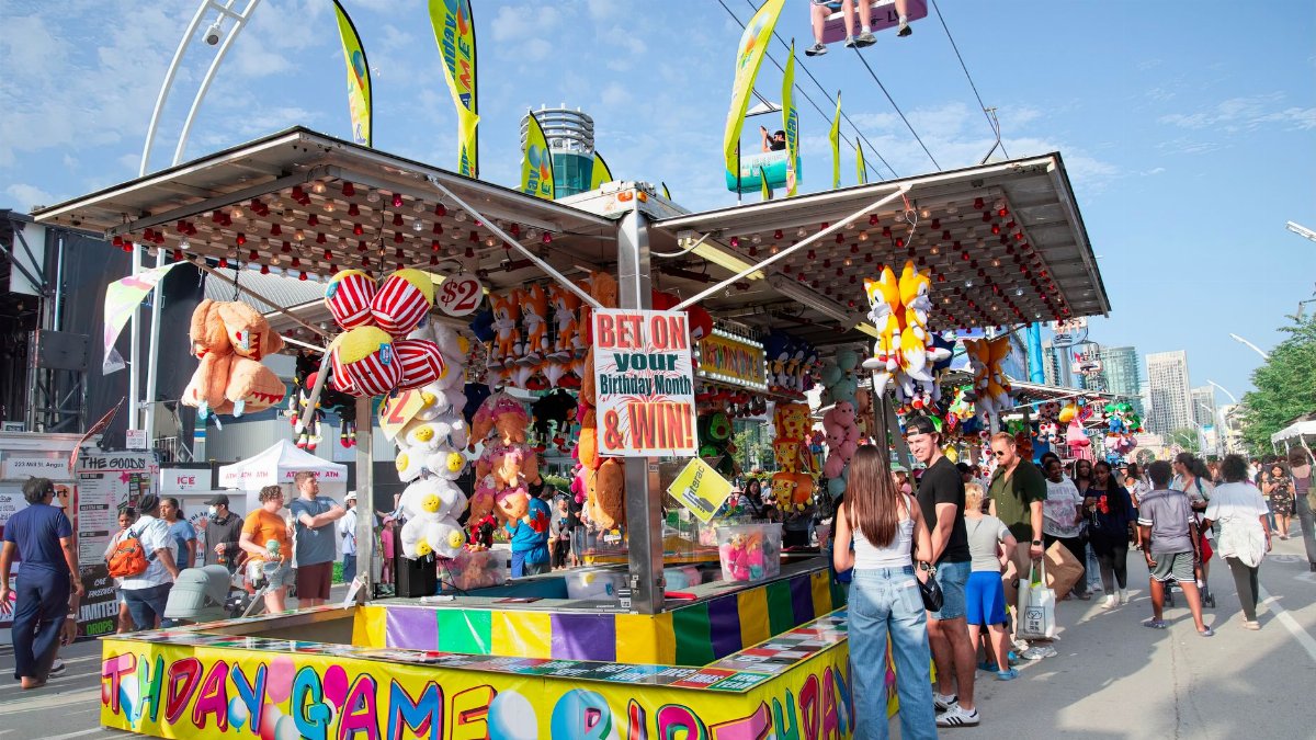 Fairgoers enjoy a vibrant carnival game booth at a Toronto fair with plush prizes and fun activities.
