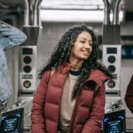 Crop cheerful ethnic woman in outerwear speaking with male partners while passing through turnstiles in subway