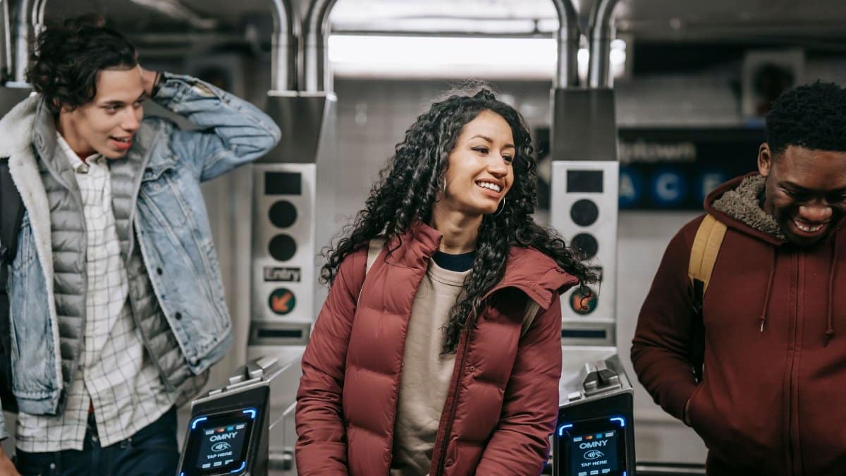Crop cheerful ethnic woman in outerwear speaking with male partners while passing through turnstiles in subway
