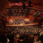 A large audience enjoys a symphony orchestra performance at the iconic Sydney Opera House.