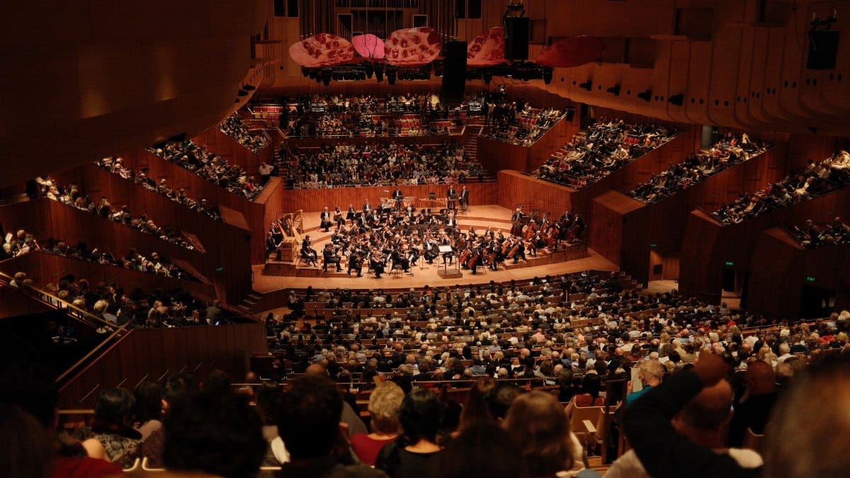 A large audience enjoys a symphony orchestra performance at the iconic Sydney Opera House.