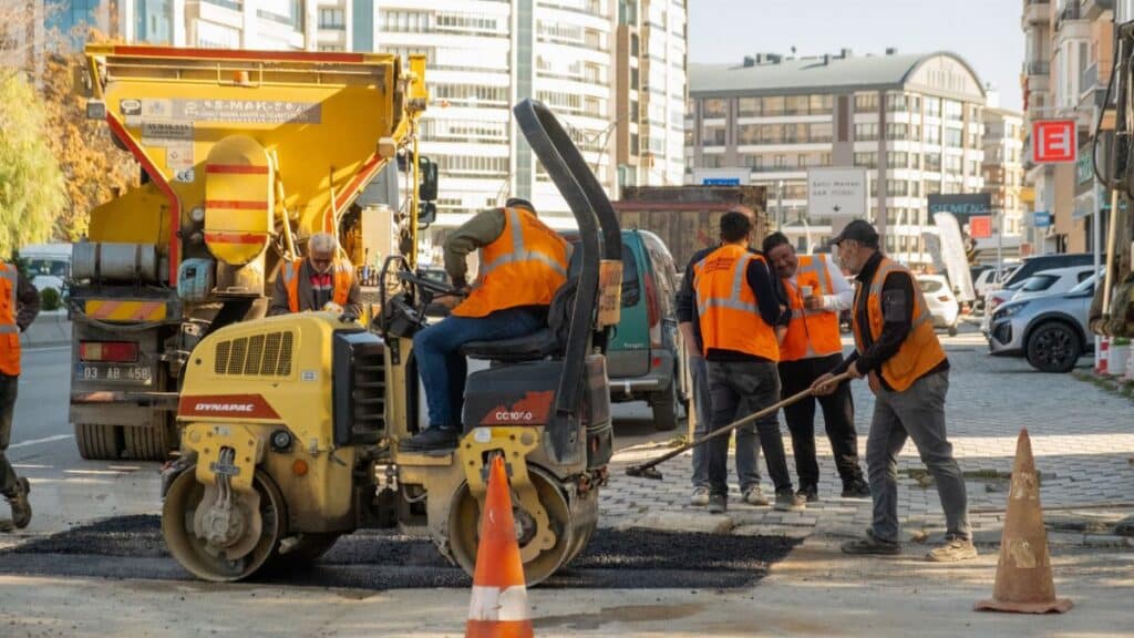 Construction workers in orange vests repair city road with vehicles during the day.