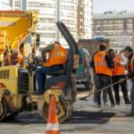 Construction workers in orange vests repair city road with vehicles during the day.