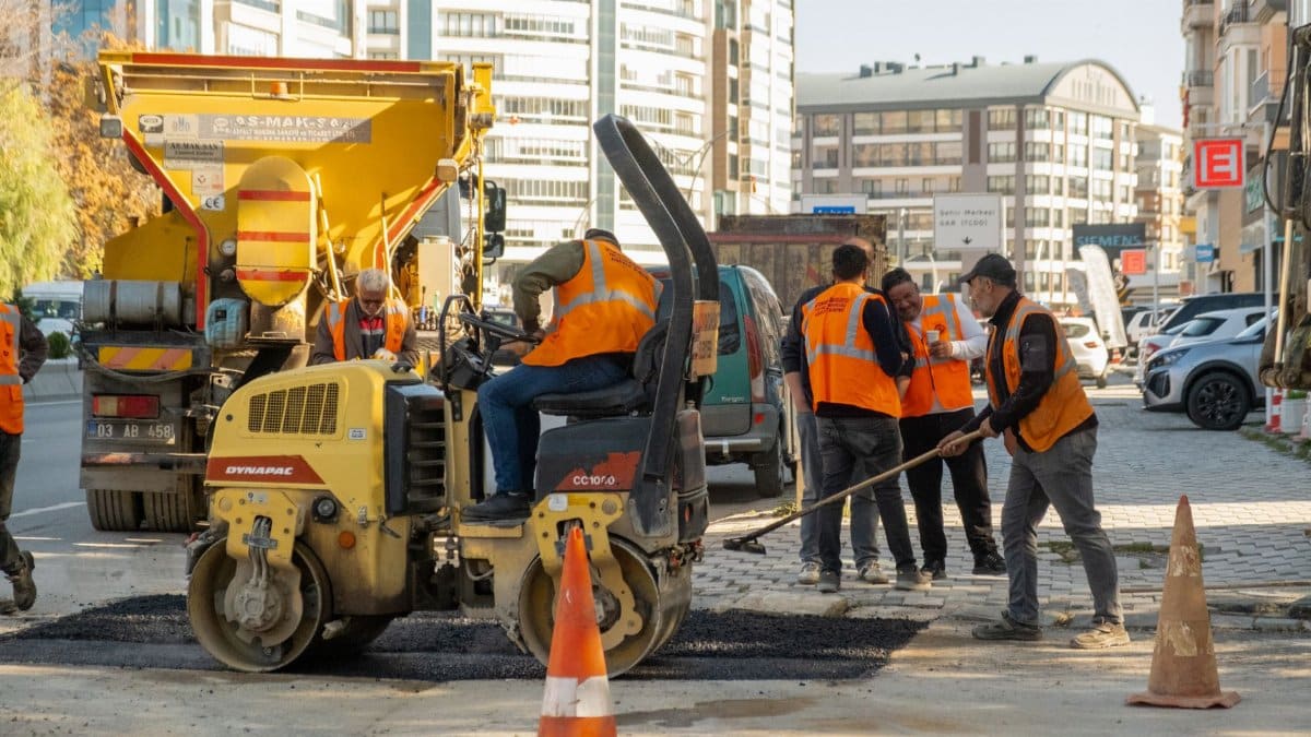 Construction workers in orange vests repair city road with vehicles during the day.