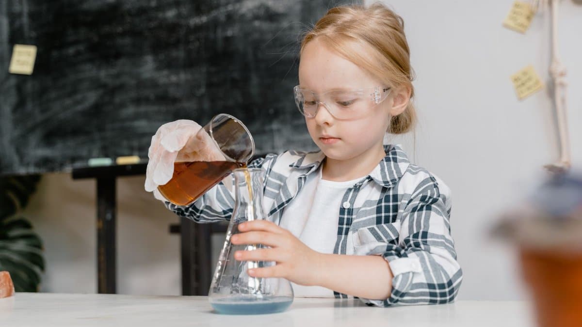 A young girl in safety goggles pouring liquid in a classroom science experiment.
